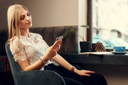 Happy young woman using her smartphone while sitting in cafeteria