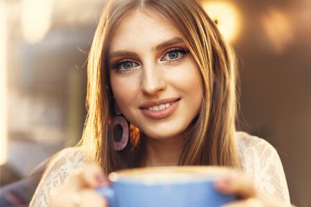 Portrait of a young woman having a cup of coffee and looking through the windowの写真素材
