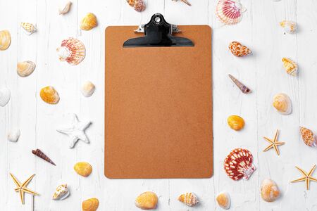 Clipboard with sea shells on wooden table close up, copy space