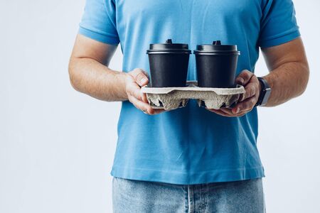 Man coffee shop worker giving takeaway cups of coffee on grey backgroundの写真素材