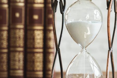 Vintage hourglass against a stack of old books close up