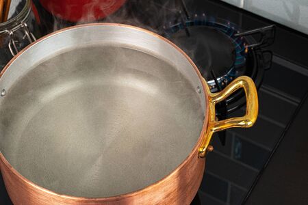 Copper pot with boiling water on a gas stoveの写真素材