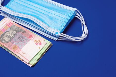 Medical face mask and Ukrainian hryvnia banknotes on blue background
