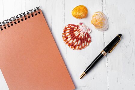 Open notepad with sea shells on white wooden background, top view