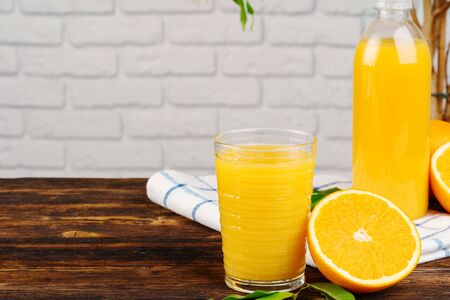 Bottle of fresh orange juice on wooden table against white brick wall backgroundの写真素材