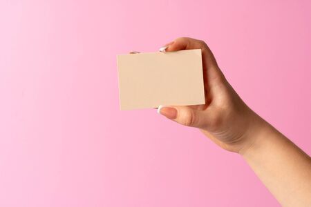 Woman hand showing blank business card on pink background. Close up.