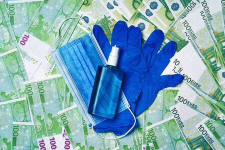 Protective medical mask, gloves and sanitizer on a background of Euro banknotesの写真素材