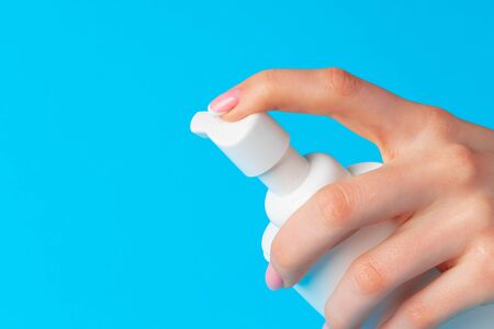 Female hand holding skincare product bottle on blue backgroundの写真素材