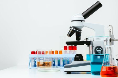 Microscope and colored test tubes on table in laboratory, close up