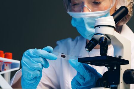Woman scientist looking at slide with blood sample near microscope in laboratoryの写真素材
