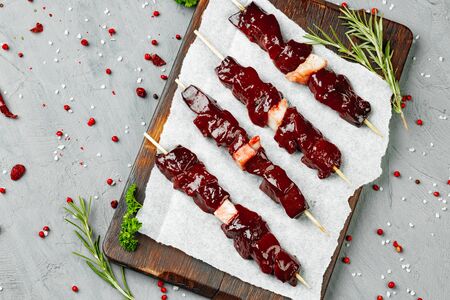 Raw liver kebab on skewers on wooden board