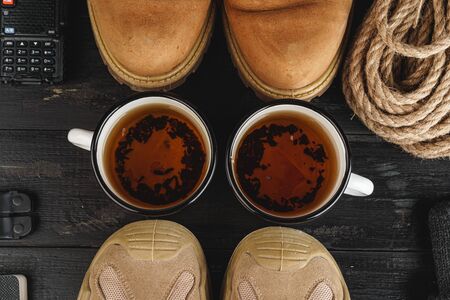 Hiking boots with equipment for hiking, cup of tea on wooden board