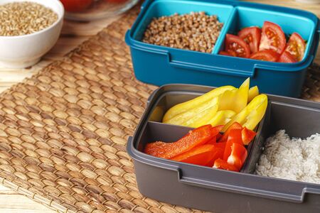 Two lunch boxes with cooked groats and cut vegetables, close up