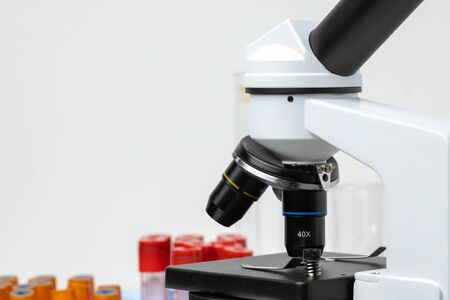 Microscope and colored test tubes on table in laboratory, close up