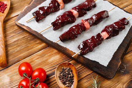 Raw liver kebab on skewers on wooden board