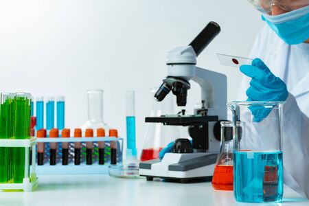 Woman scientist looking at slide with blood sample near microscope in laboratoryの写真素材
