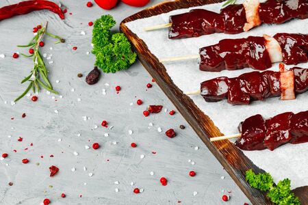 Raw liver kebab on skewers on wooden board