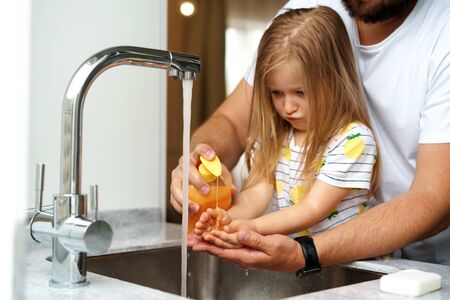 Father and daughter washing their hands above the sink in a kitchenの写真素材