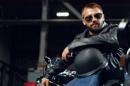 Portrait of bearded man motocyclist in dark sunglasses on dark backgroundの写真素材