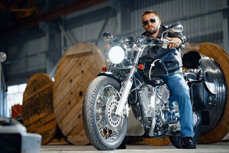 Bearded motorcyclist in black leather clothing with his motorbike