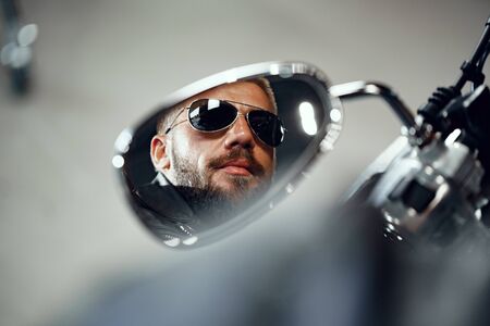 Reflection in the motorcycle mirror of a man driver in sunglasses