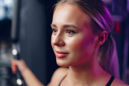 Close up portrait of a young blonde woman in sport bra in a dark gym