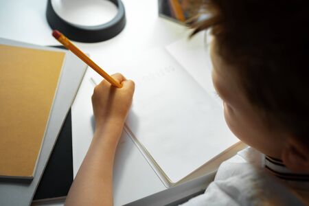 Little boy writing something in his notebook close up