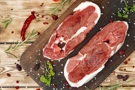 Raw meat steaks with herbs on wooden board close upの写真素材