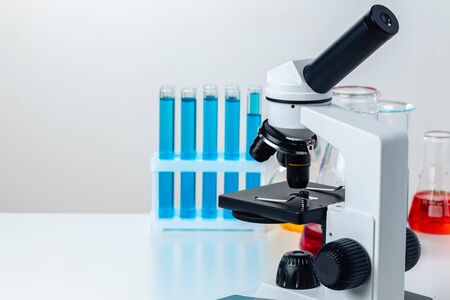 Close up of laboratory microscope with set of test tubes with blue liquid for research