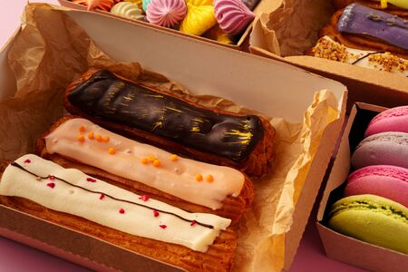 Box with fresh eclairs on pink background close up