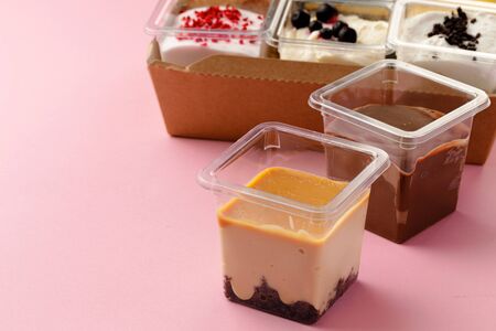 Mousse desserts in square plastic boxes with different toppings on pink table, copy spaceの写真素材