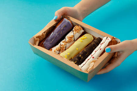 Womans hands holding a box with fresh eclairs on blue backgroundの写真素材