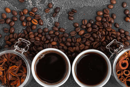 White coffee cup with with beans on dark surface close up