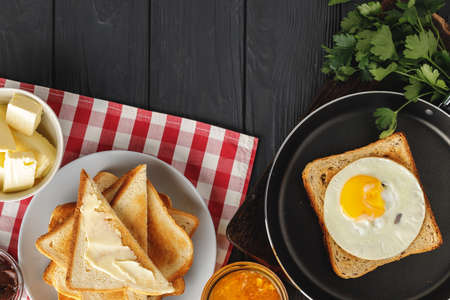 Fried egg in frying pan with sliced bread on black wooden table