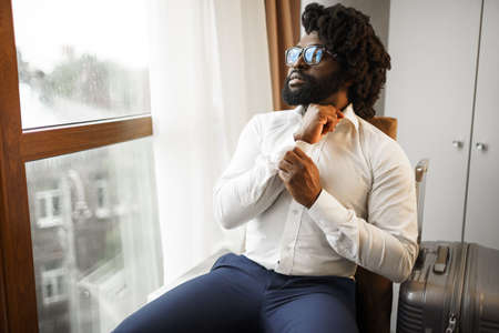 Black man businessman sitting and looking at window in hotel roomの写真素材