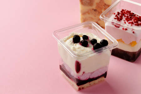 Mousse desserts in square plastic boxes with different toppings on pink table, copy space