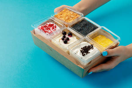Mousse desserts in square plastic boxes with different toppings on pink tableの写真素材