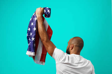 Back view of a black man holding USA flag against turquoise backgroundの写真素材