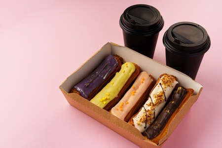 Box of eclairs with takeaway coffee cups on pink background, copy space