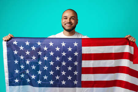 Portrait of young dark-skinned man proudly holding USA flag