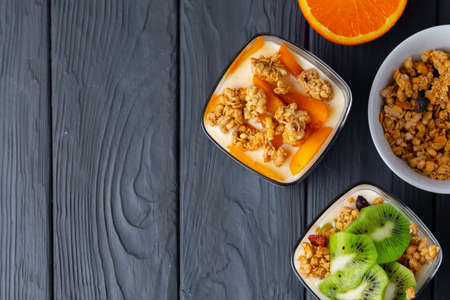 Tasty breakfast with granola, yoghurt and fruits in a glass bowl on wooden tableの写真素材