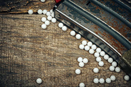 Close up of airsoft gun magazine and airsoft balls on wooden background