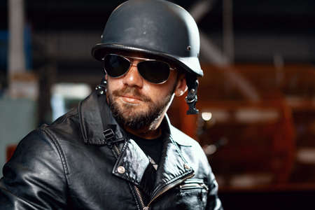 Portrait of bearded man motocyclist in dark sunglasses on dark backgroundの写真素材