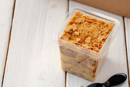 Creamy dessert in a plastic box on wooden table close up