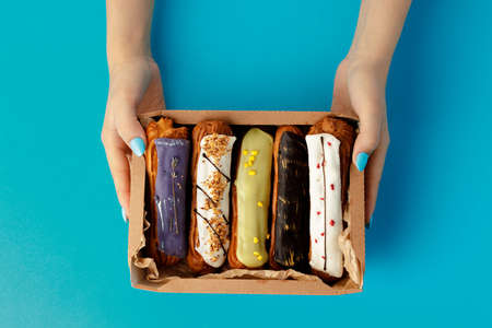 Womans hands holding a box with fresh eclairs on blue background