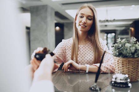 Young beautiful woman hotel guest paying for her stay with credit card at front deskの写真素材