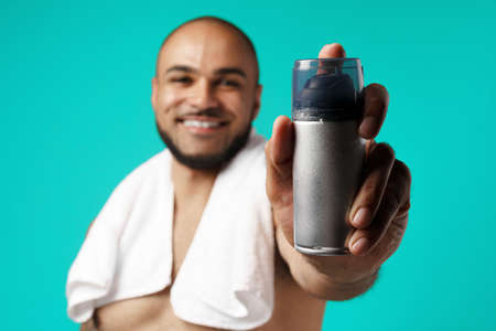 Happy african american man with towel holding shaving foamの写真素材