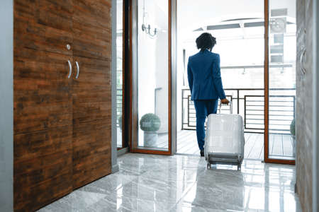 Black man in formal suit with packed suitcase entering hotel doorの写真素材