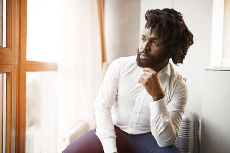 Black man businessman sitting and looking at window in hotel roomの写真素材