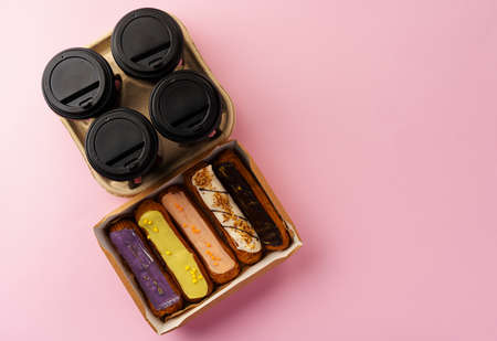 Box of eclairs with takeaway coffee cups on pink backgroundの写真素材